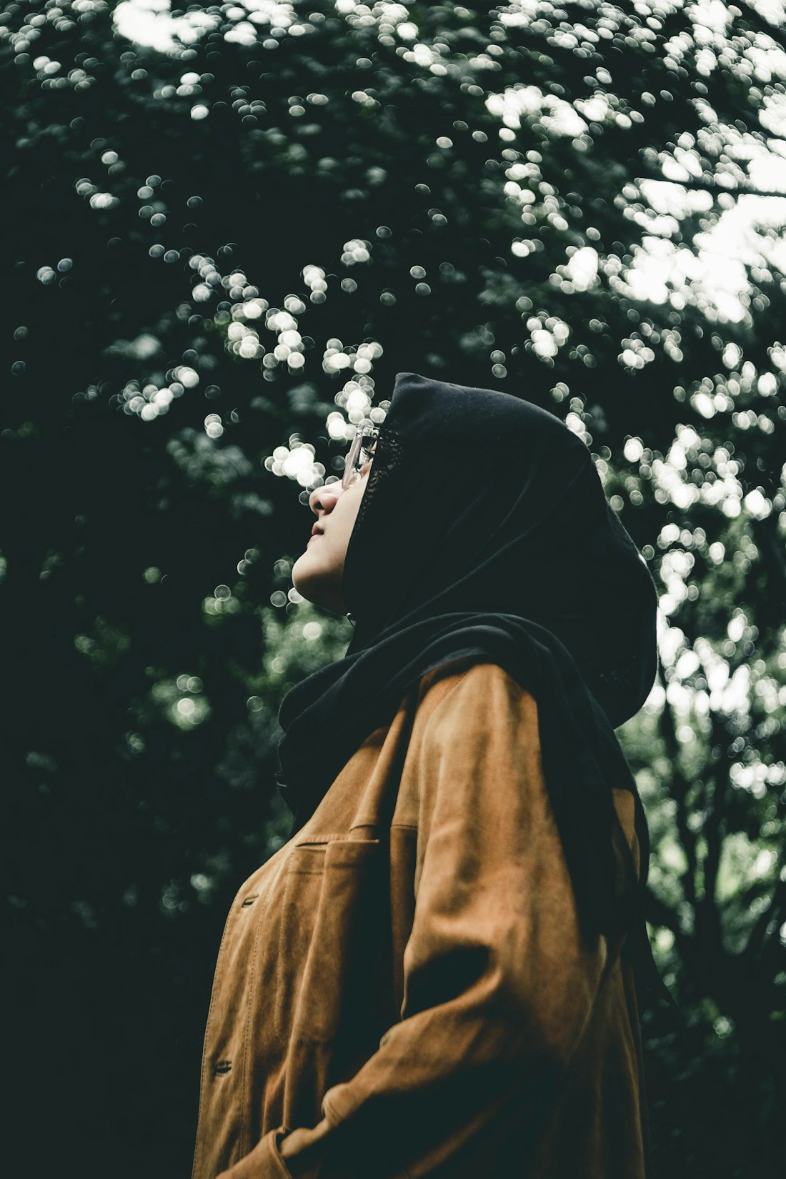 Young woman in a hijab and mustard jacket looking up thoughtfully